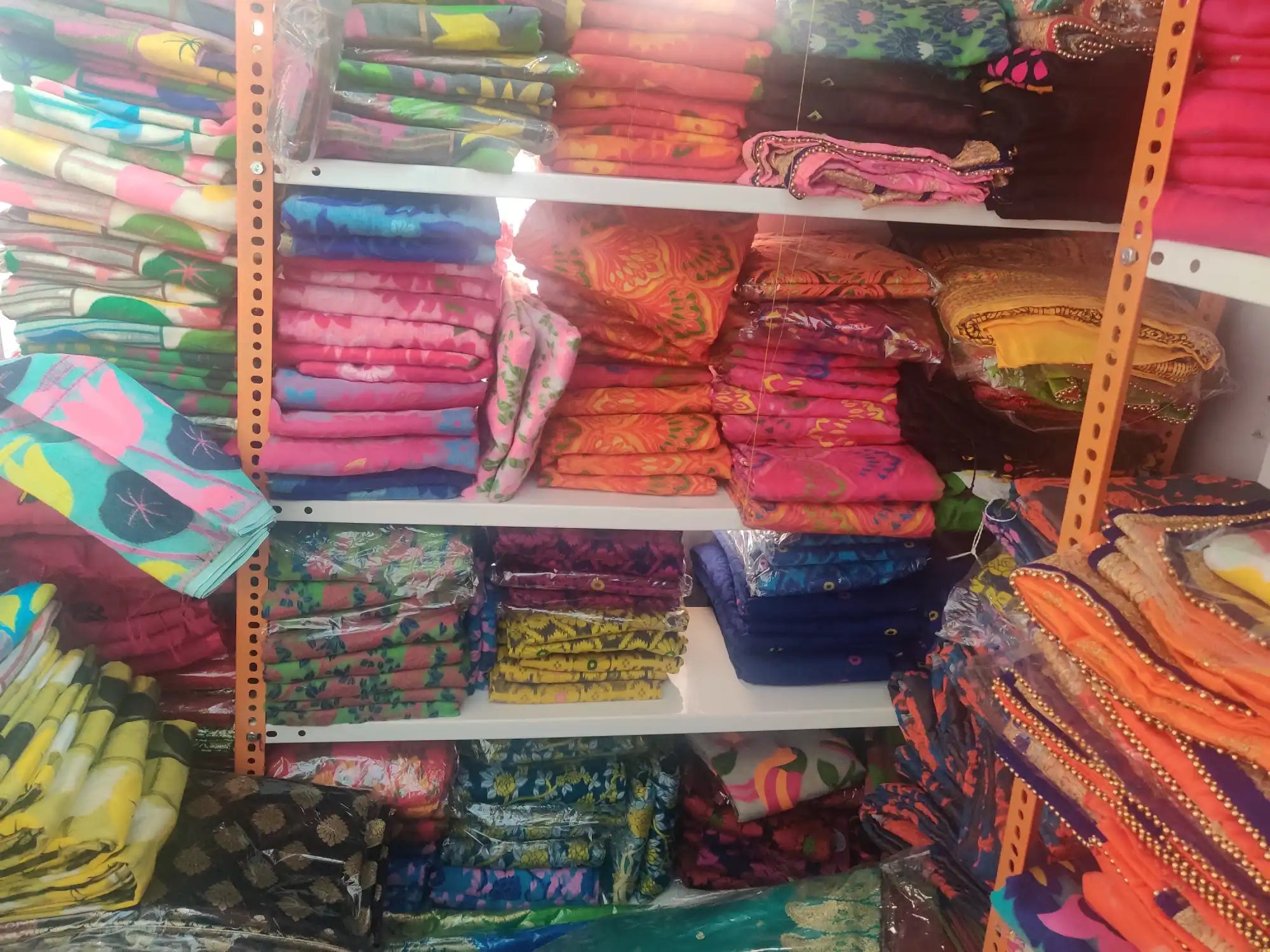 Colorful stacks of folded fabrics arranged on retail shelving.